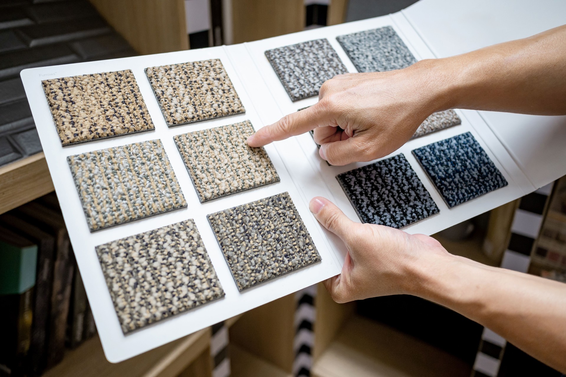 Designer hand pointing at sample fabric pieces on carpet swatch collection. Customer choosing color sample from rug catalog for interior floor finishing material in home design store