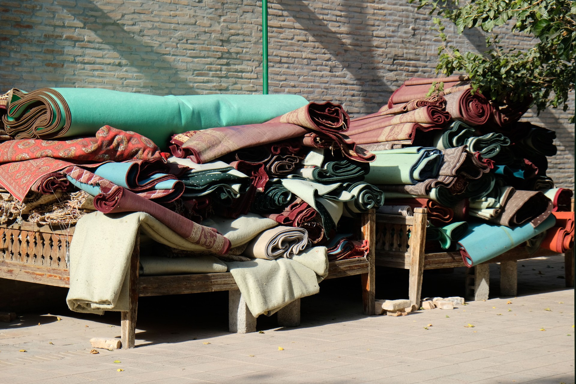 Colorful carpets stacked on wooden benches in a bustling market setting during a sunny day